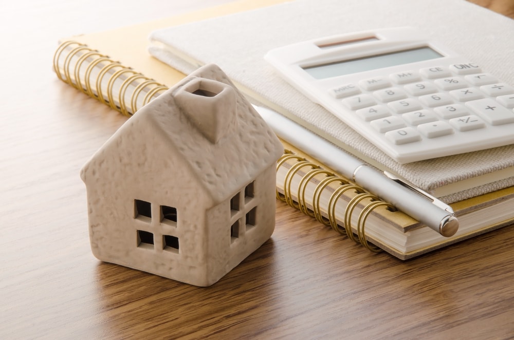 Small model house beside a calculator, pen and notebooks on a desk